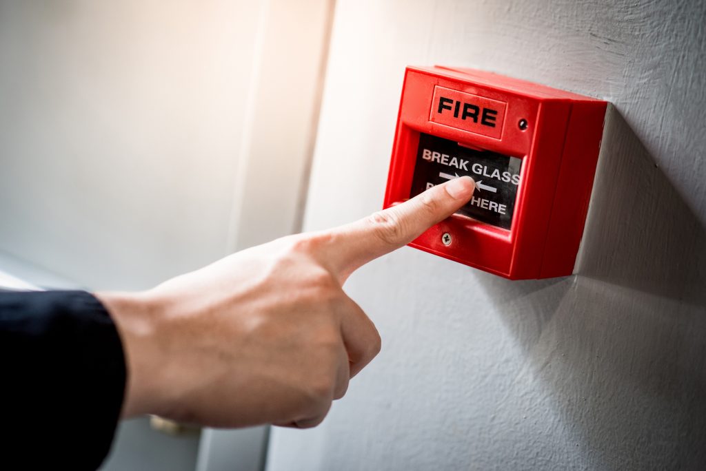 Male hand pointing at red fire alarm switch Astra Security Systems